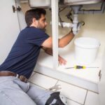 Plumber fixing under the sink in the kitchen